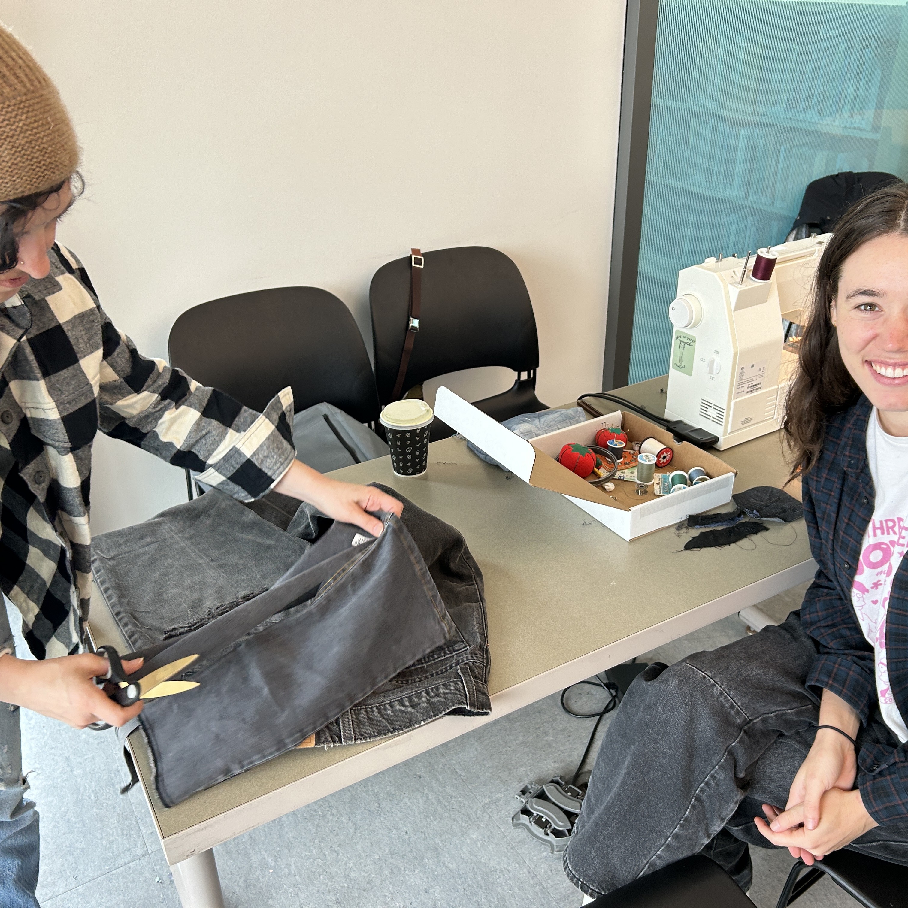 Two people are working on a clothing item with a sewing machine and scissors