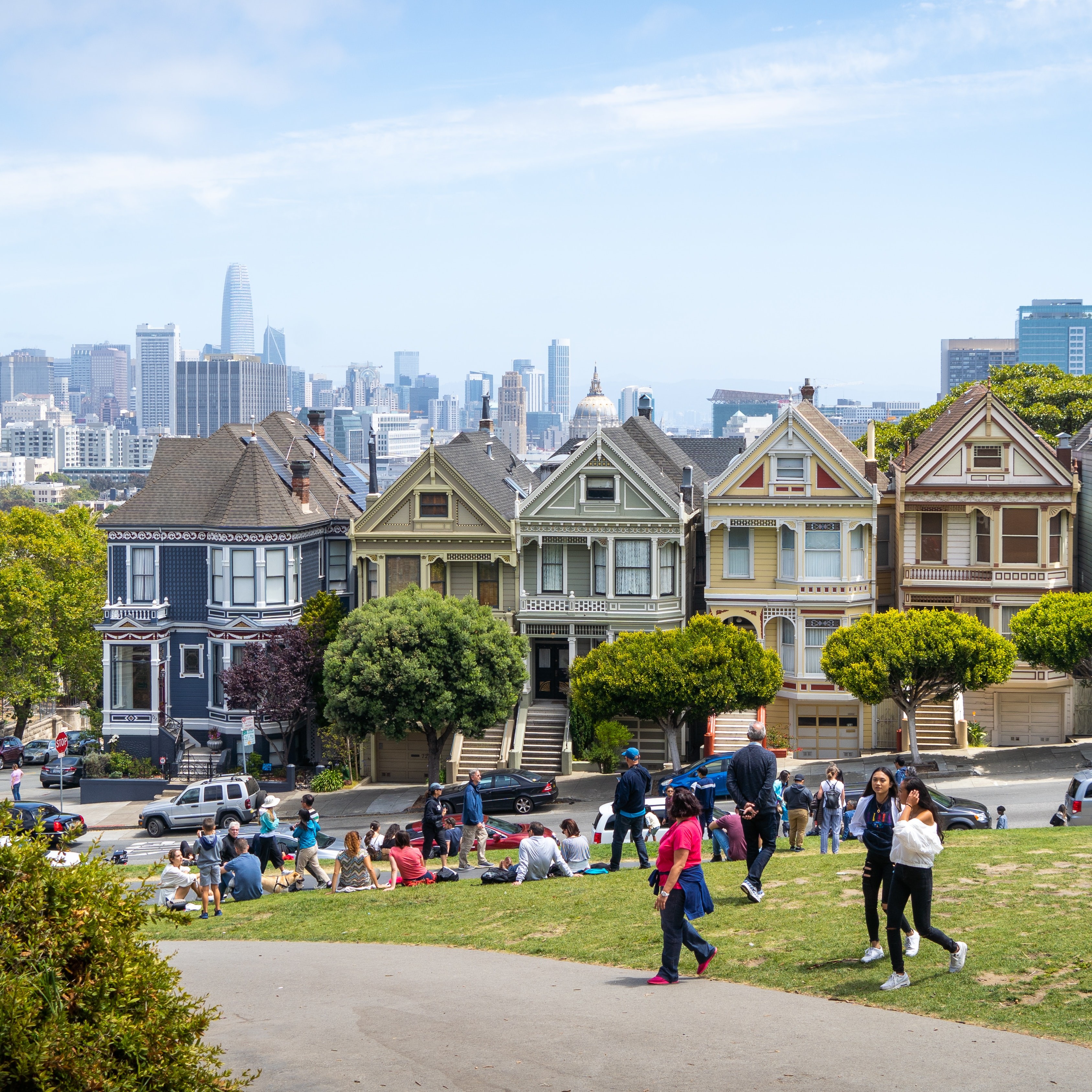 San Francisco's famous "Painted Ladies" Victorian homes are shown in the background with people relaxing and socializing at the park in the foreground
