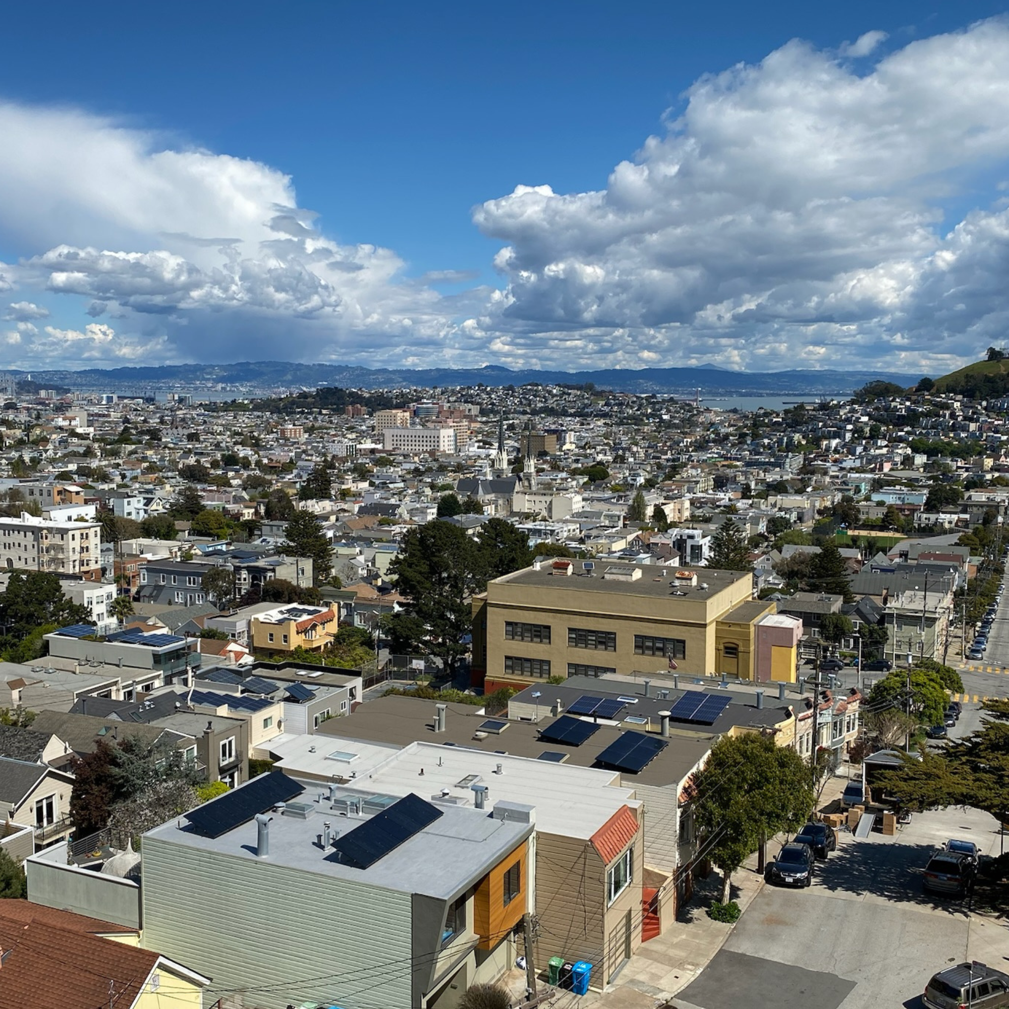 A view of the city of San Francisco with a hill to the far right of the image and the tops of residential buildings and homes in the foreground