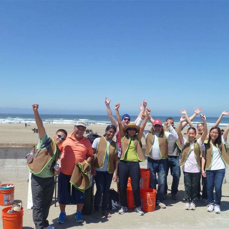 Volunteers cheer together after cleaning up Ocean Beach with the ocean behind them.