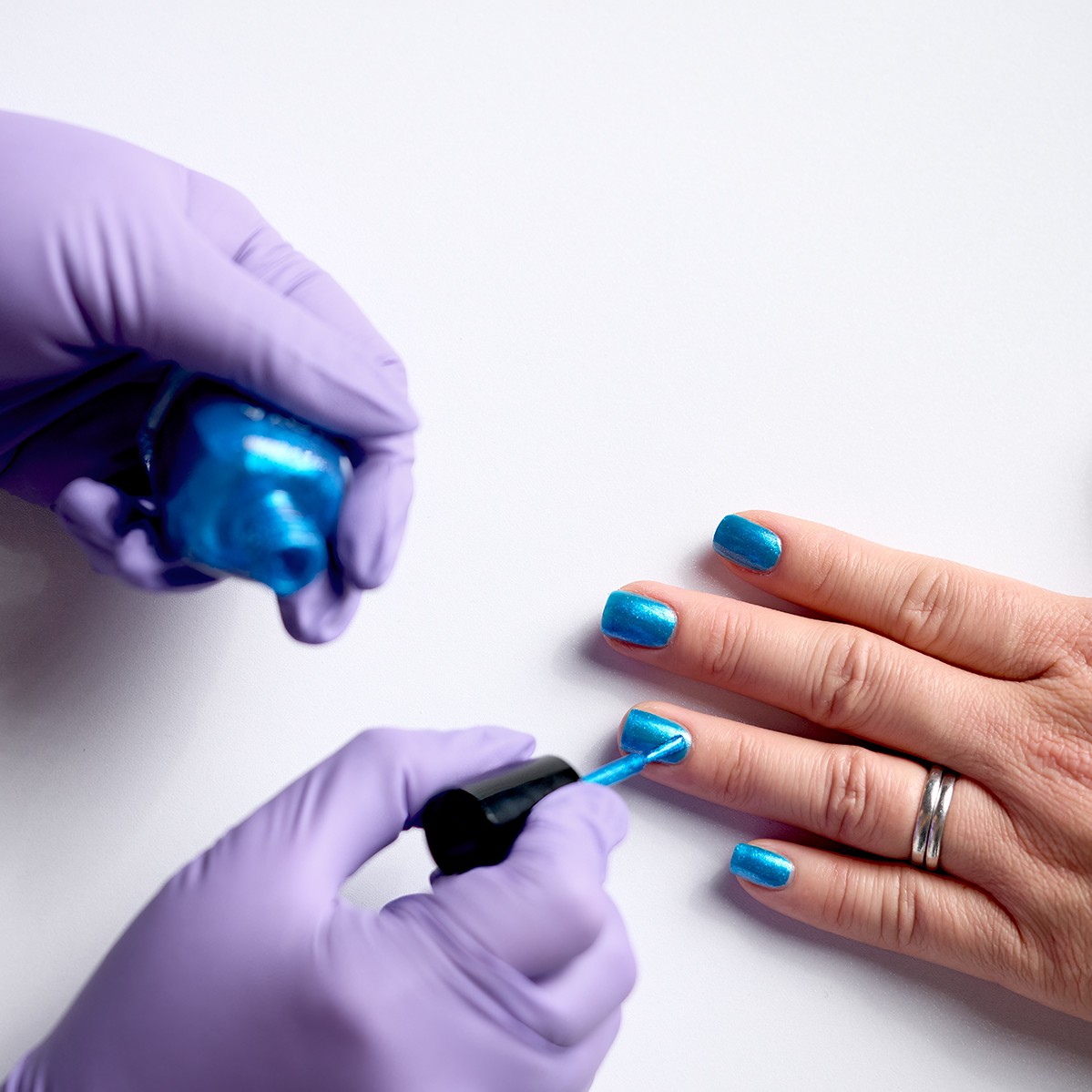 Two gloved hands applying blue nail polish on another set of hands. 