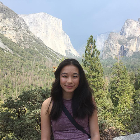 Woman smiling with black hair wearing purple top. Yosemite Valley in background
