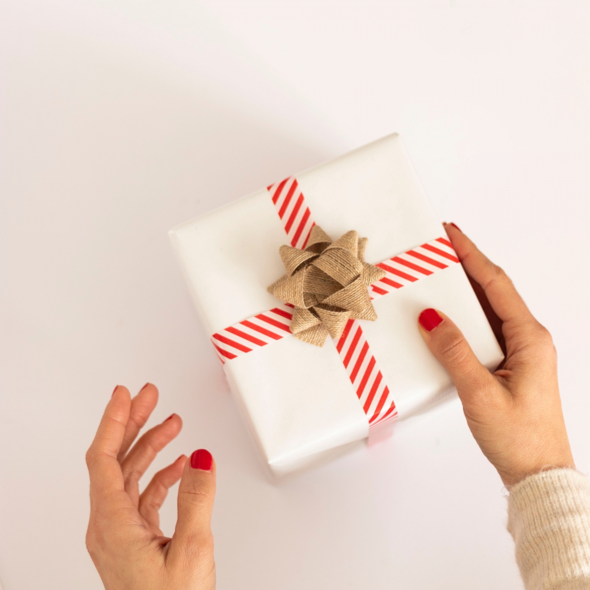one hand holding white box gift with brown bow, other hand in air