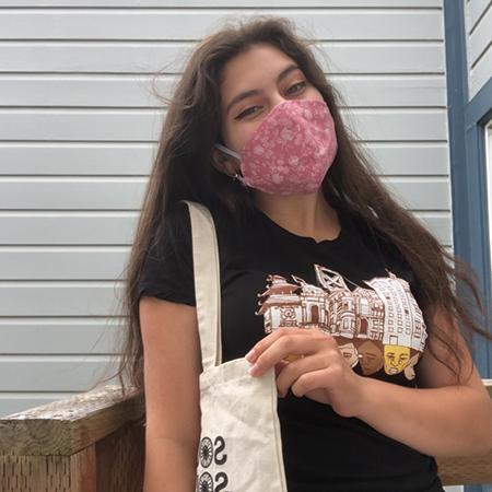 Young teenager with long brown hair wearing pink flower mask, black shirt, with canvas tote over shoulder