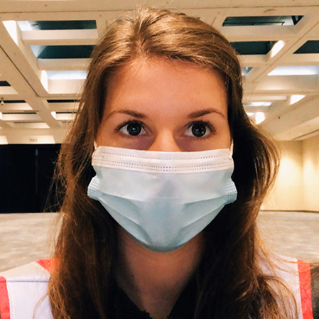 Women with hair on shoulder, wearing blue mask looking forward with white and red attire