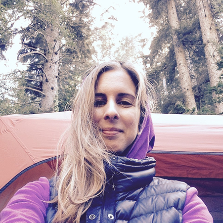 woman in black puffy best and purple sweatshirt looking at camera smiling with trees in background