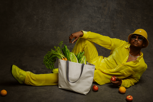 Landscape portrait of person wearing an all-yellow outfit and hat with a reusable bag with groceries in the foreground