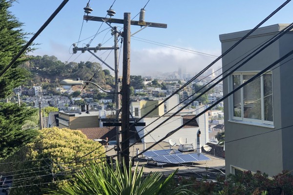Power lines in a San Francisco neighborhood. Trees are to the right and a grey apartment building to the left. 