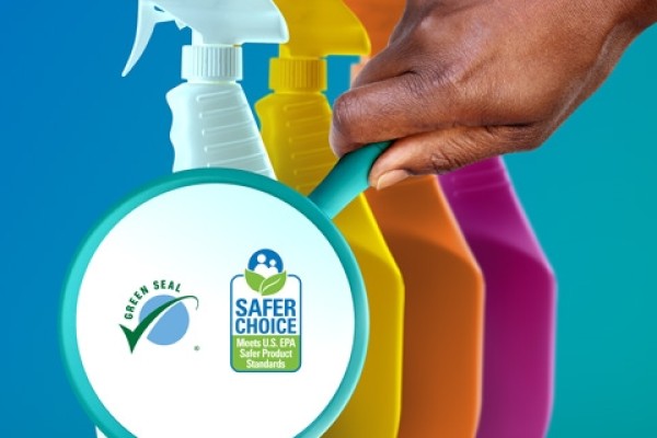 Four multi-colored spray bottles in a row with a hand holding a magnifying glass over the first one