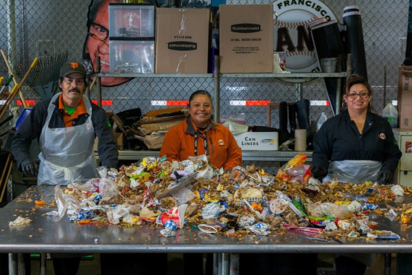 Three volunteers are standing next to a large aluminum table with trash scraps on top