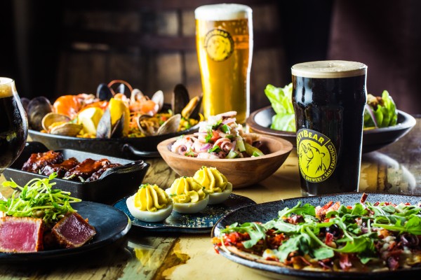 A table with various dishes of food, salas, seared tuna, deviled eggs, and two pints of beer. All drink and food are presented on the table in reusable plates, bowls, and cups