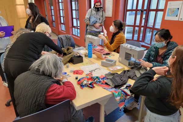 A community event, sewing clothes to repair them, around a table