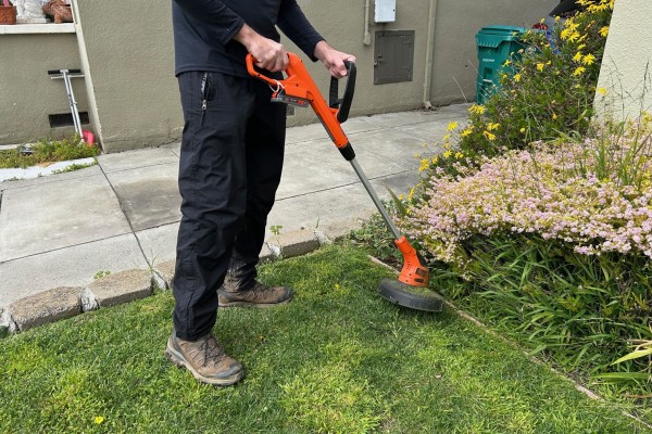 a person wearing all black using an electric weed eater