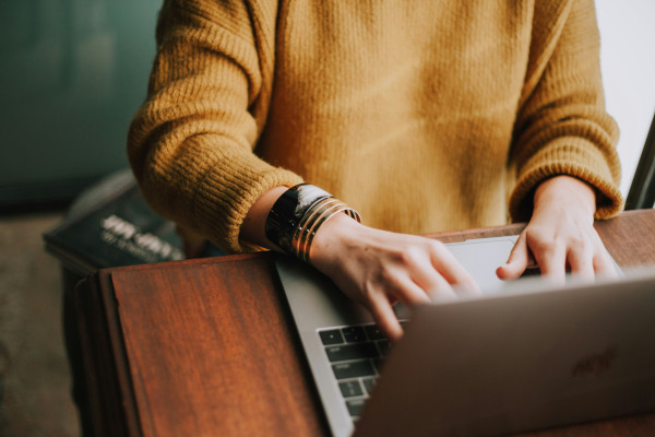 Someone seated at a desk typing on their laptop wearing a yellow sweater