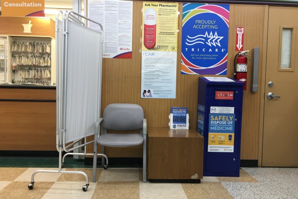 The inside of a pharmacy shows a mobile privacy curtain a grey chair and small table