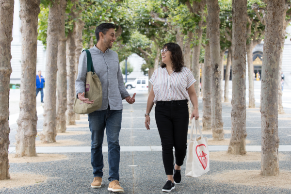 Two people walking in front of SF City Hall with reusable bags