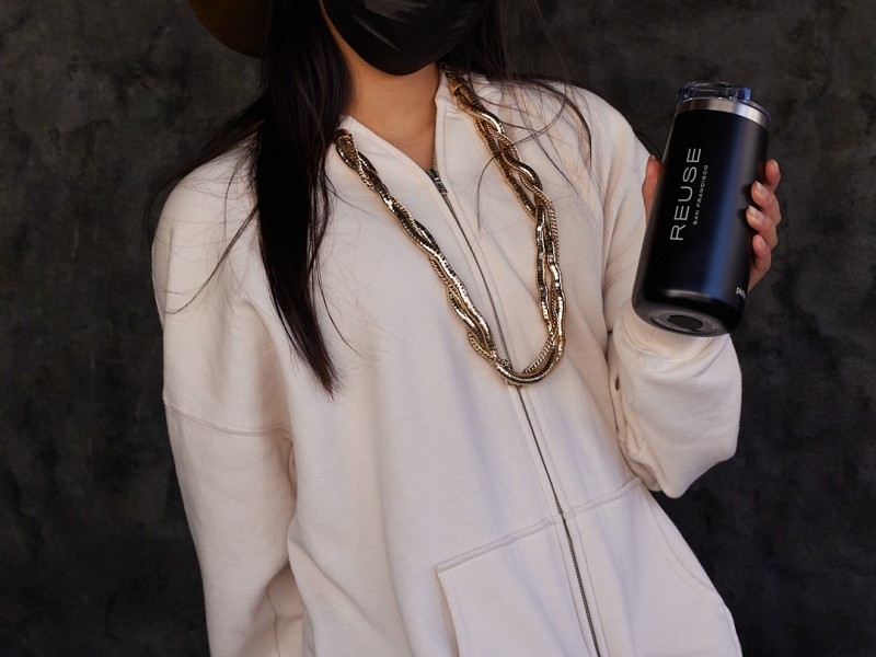 A person wearing a brown hat and black mask poses with a reusable water bottle