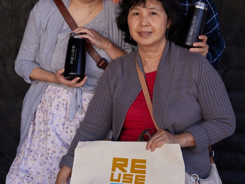 Three individuals pose with their reusable water bottle and shopping bag