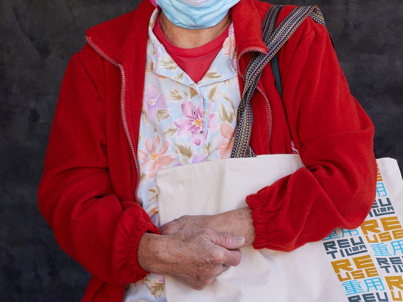An older woman wearing a purple hat and posing with the SFE reusable bag