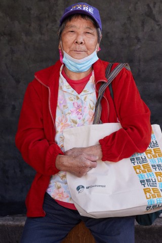 An older woman wearing a purple hat and posing with the SFE reusable bag