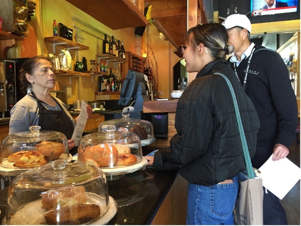 Zero Waste specialist from the Department stands at the counter of a local business speaking to an employee about Zero Waste policies