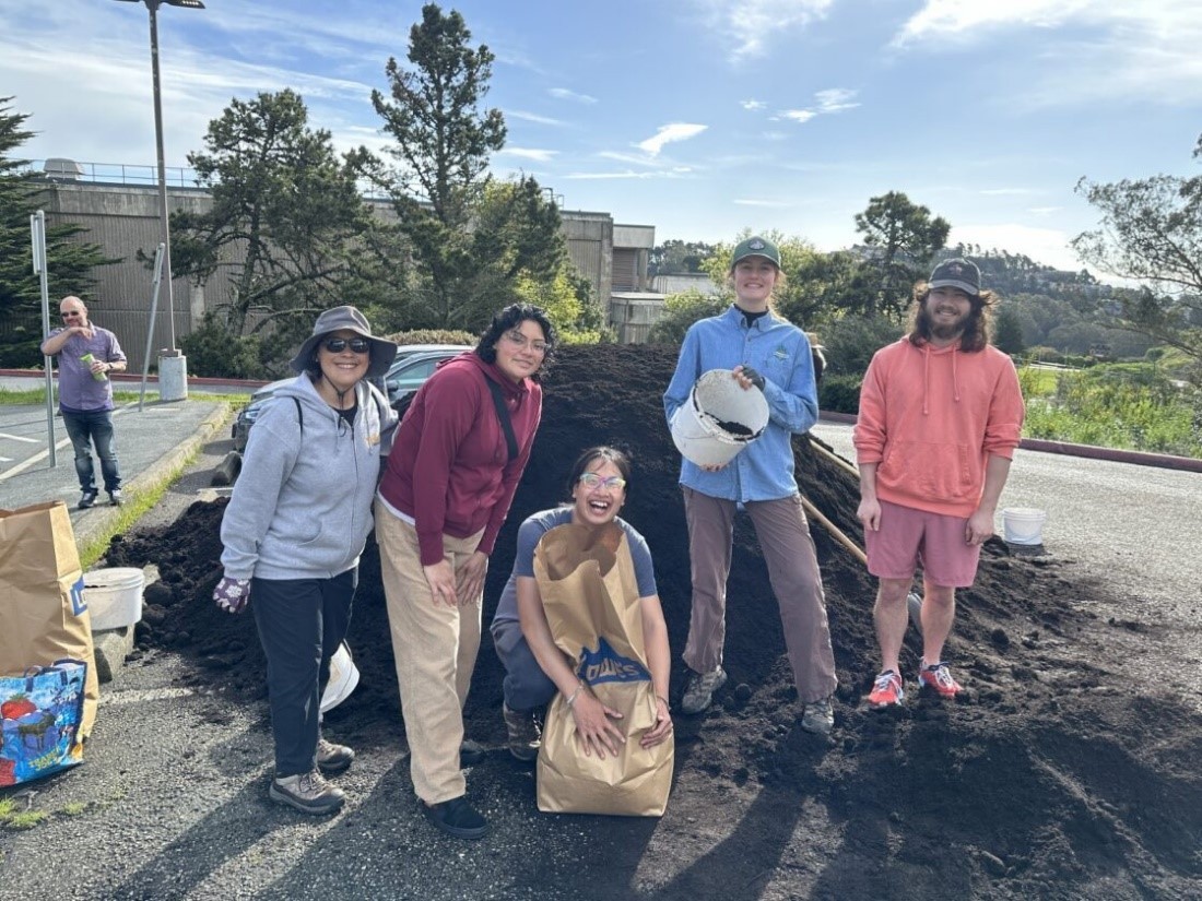 A group of five people in front of a mound of compost