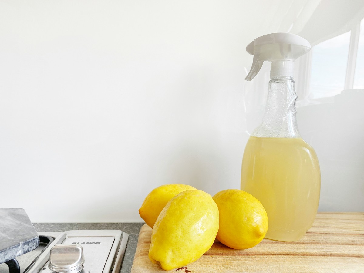 A spray bottle on a wooden desk with loose lemons beside it