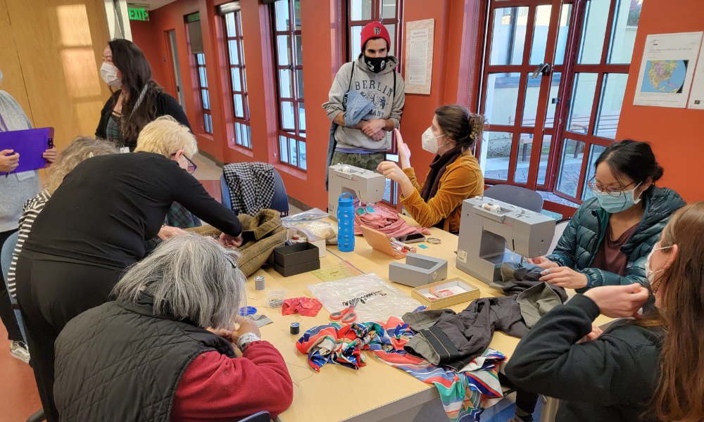 a group around a table with a few sewing machines, repairing and mending clothes