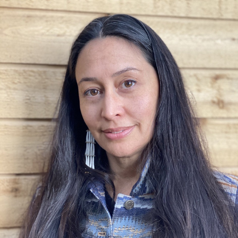 A woman with long brown hair and a stripped blue button-up shirt