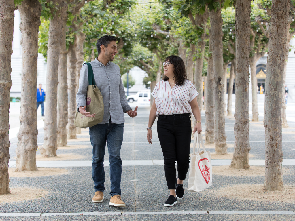 Two people walking in front of SF City Hall with reusable bags