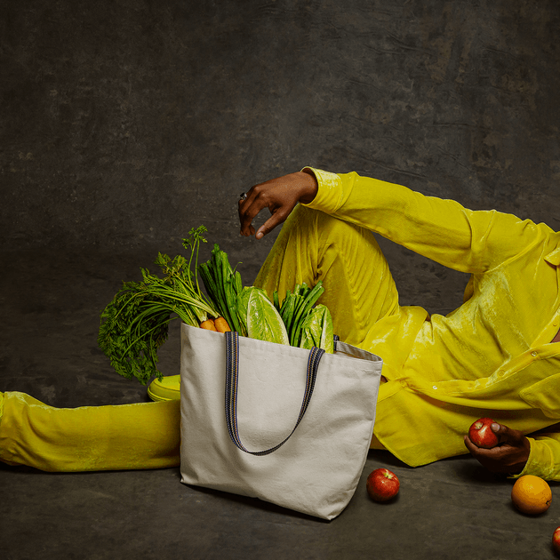 Landscape portrait of person wearing an all-yellow outfit and hat with a reusable bag with groceries in the foreground