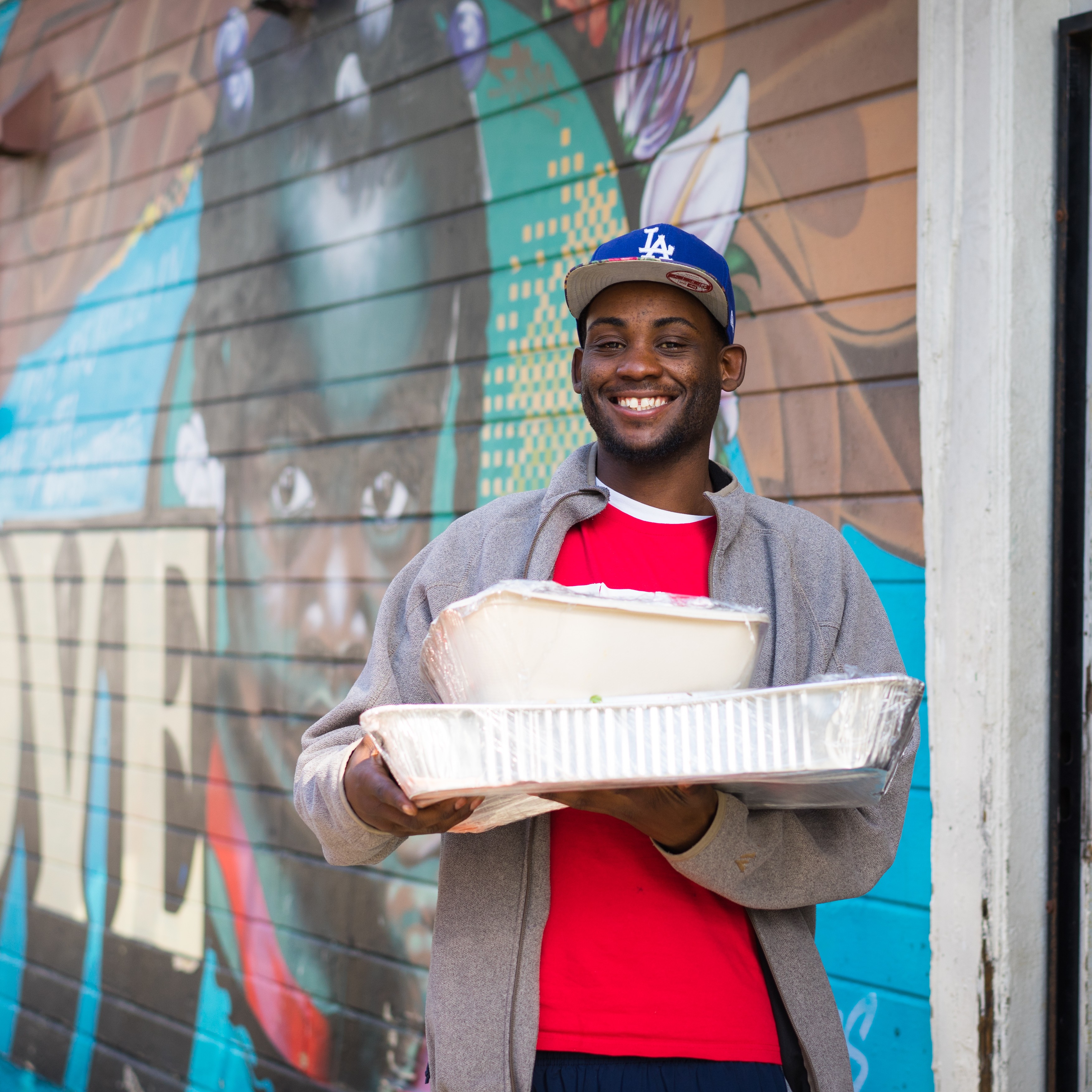 A young man smiling holding food donation trays