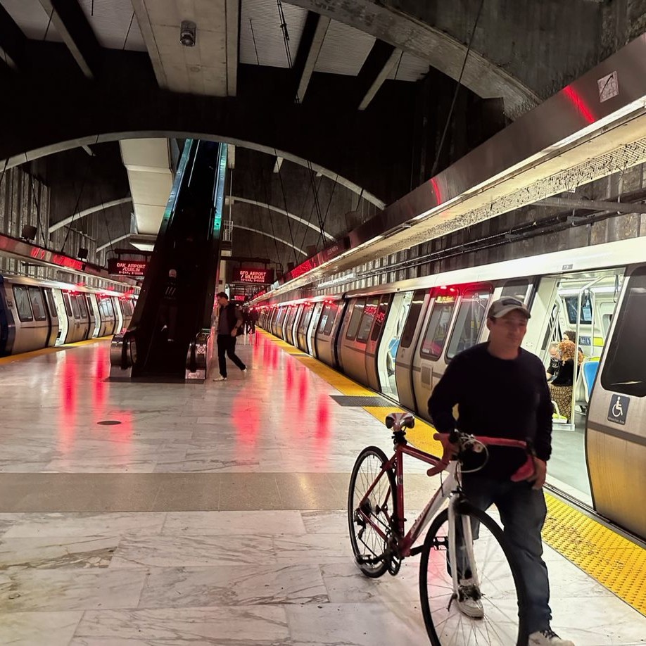 A commuter walks with his bike on the platform, next to a Bart train that is stopped at Glen Park station
