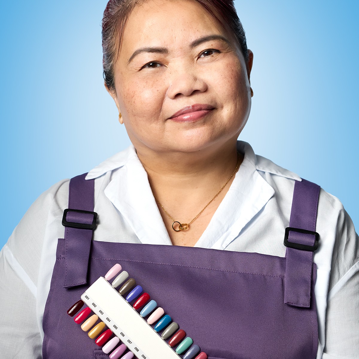 Nail salon owner wearing a purple apron and smiling into the camera