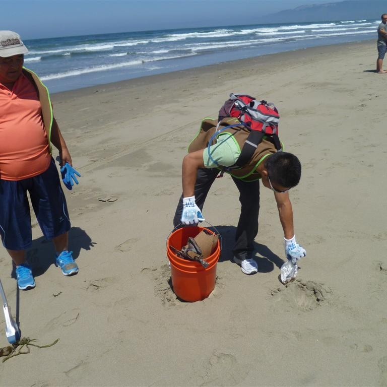 Two men pick up trash on the beach