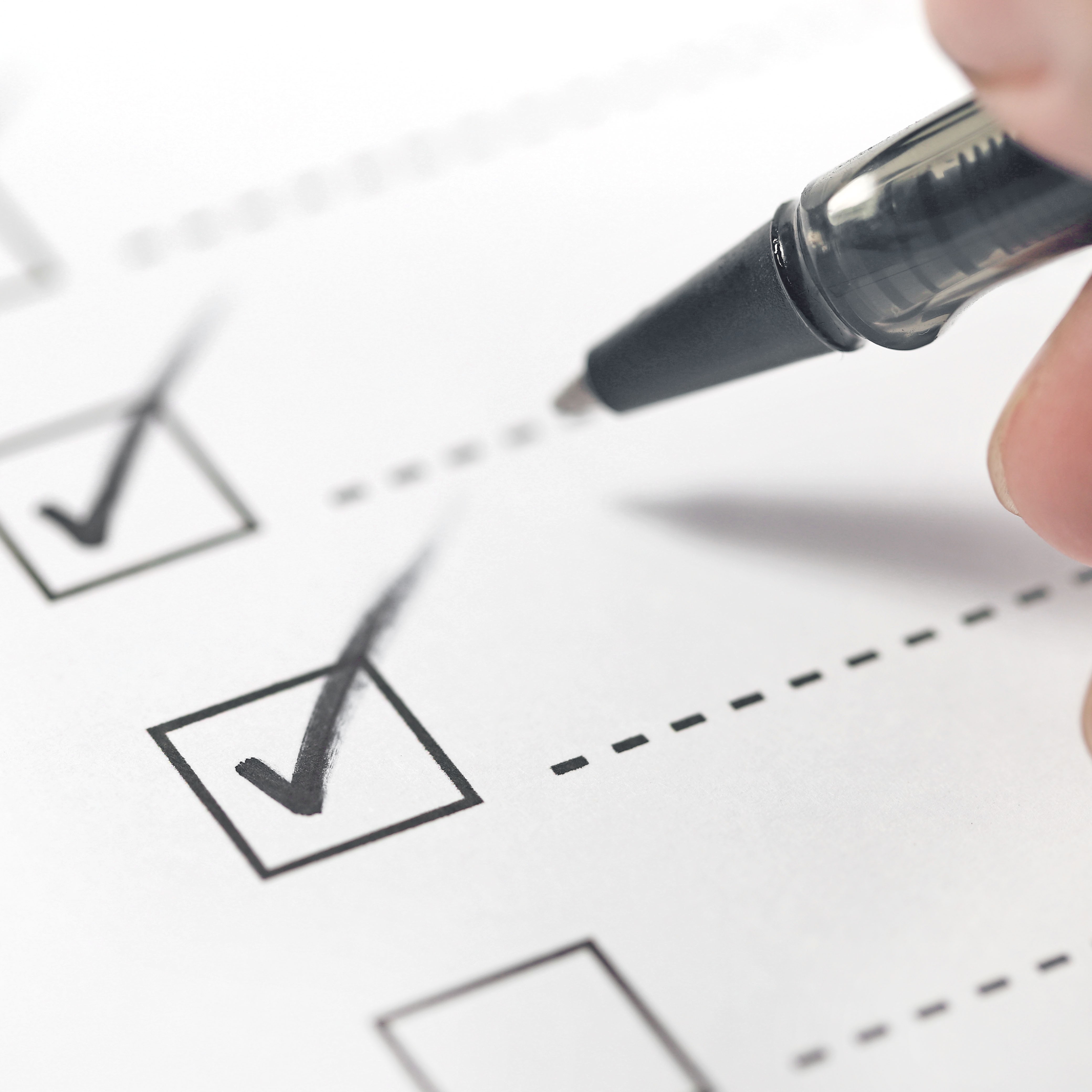 A hand holding a pen is checking off boxes on a checklist