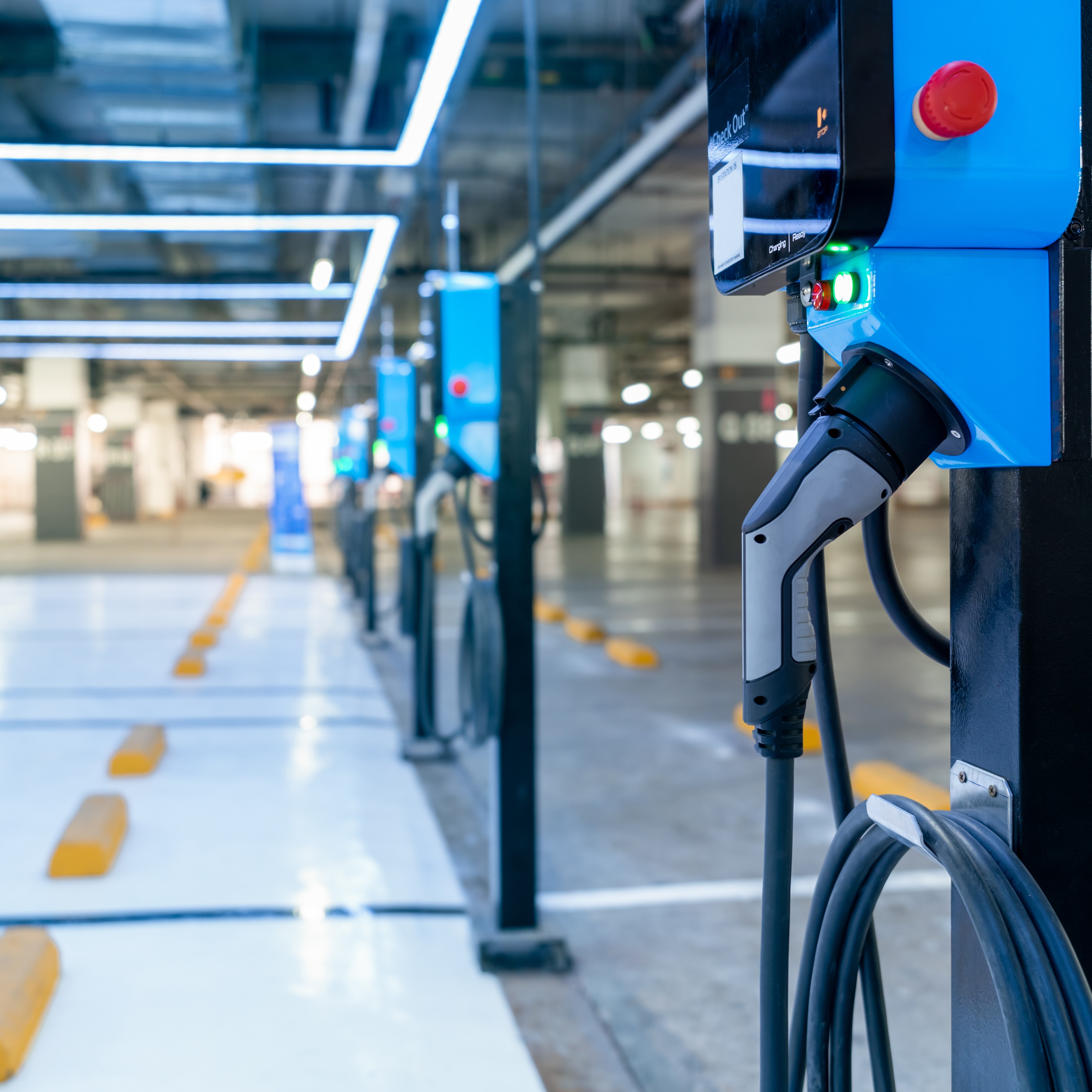 A row of electric vehicle chargers can be seen inside of a parking area of a commercial garage