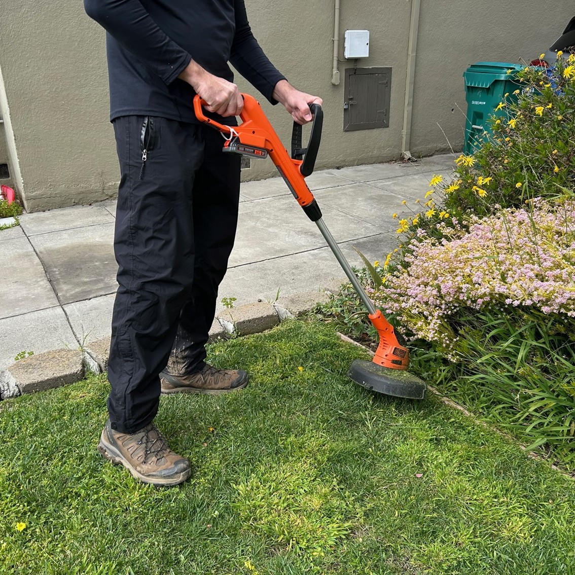 a person wearing all black using an electric weed eater