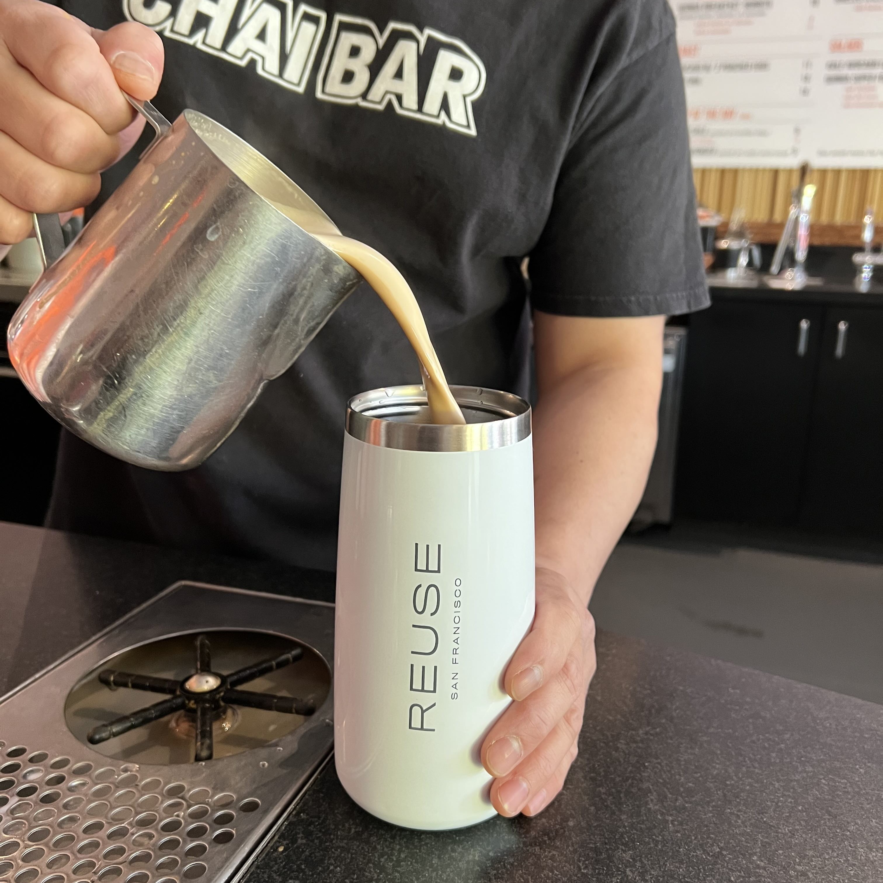 Chai tea latte being poured into a reusable mug 