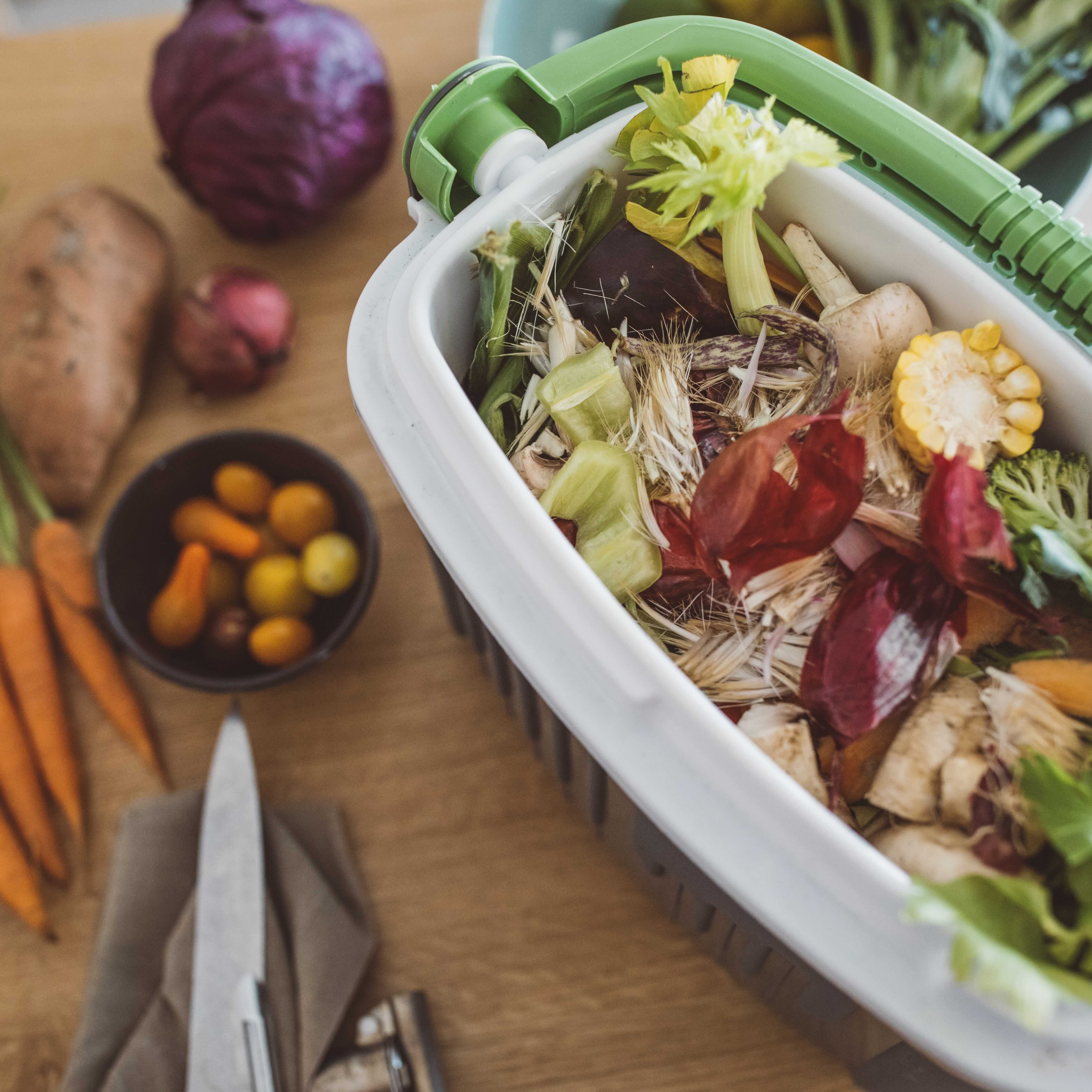 A compost pail on top of a kitchen counter with various vegetable trimmings inside