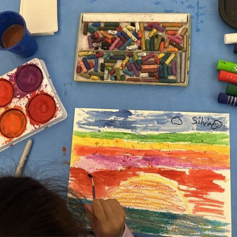 art supplies like paint and wax crayons and paper on a table 