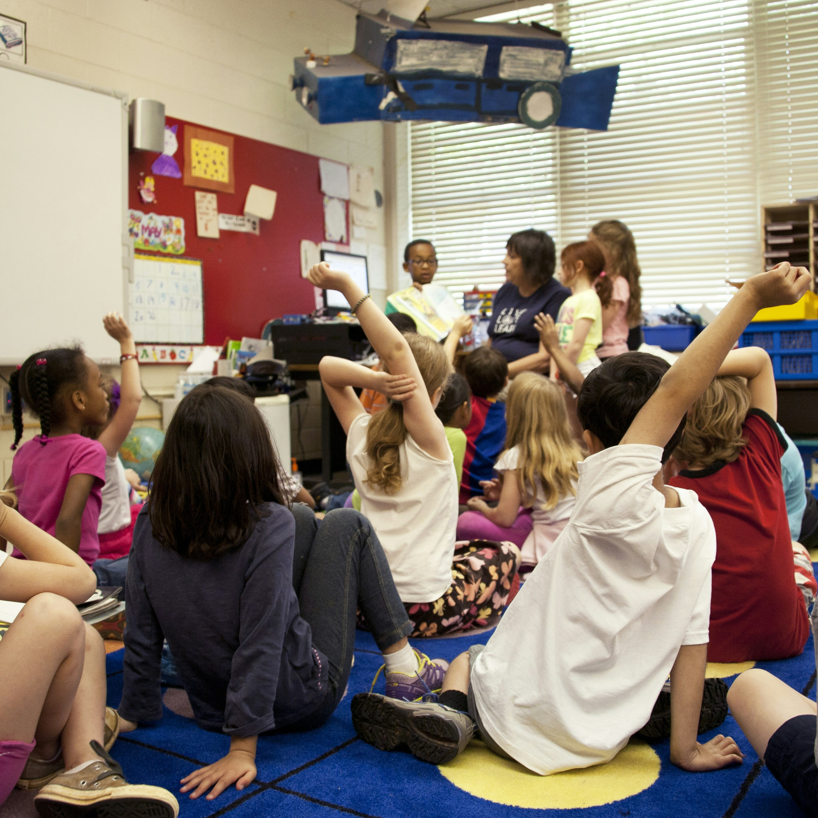 Young children raising their hands in a classroom setting