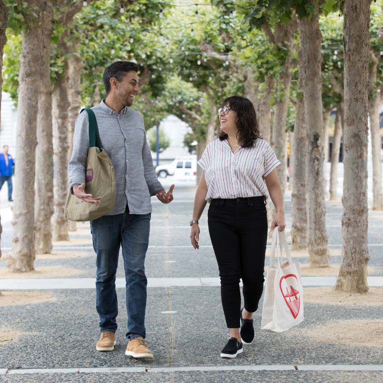 Two people walking in front of SF City Hall with reusable bags